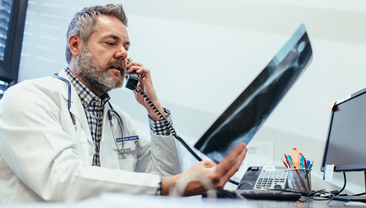 doctor-checking-x-ray-and-talking-on-telephone-at-clinic_soc