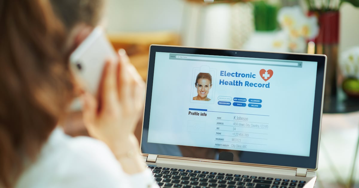 woman at home checking her medical record on a laptop while on the phone